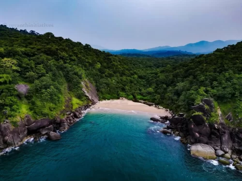 Stunning aerial drone view Butterfly Beach South Andaman misty morning, featuring horseshoe bay turquoise waters golden sand forested cliffs distant mountains, perfect Andaman paradise beach tour package. 