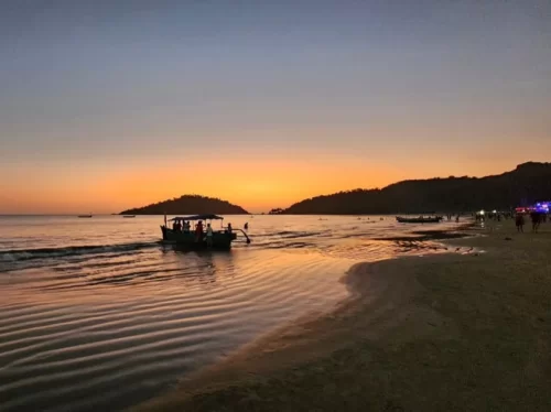 Palolem Beach Goa sunset golden sands Arabian Sea, traditional boat gliding palm hills glowing horizon, perfect Goa beach boat ride dusk package.