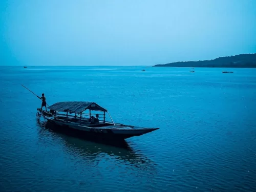 Chilika Lake Odisha traditional thatched fisherman boat silhouette blue hour distant hills serene waters, perfect Puri birdwatching dolphin safari tour package.