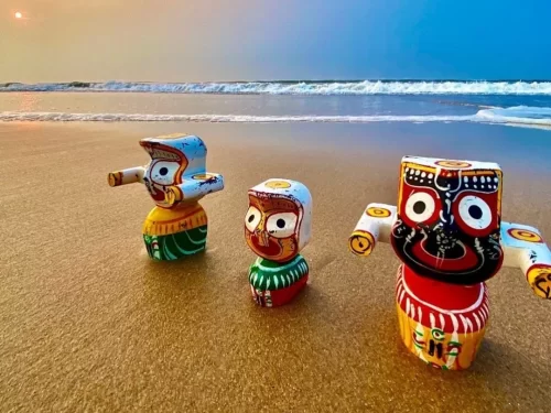 Puri Beach Odisha golden sands sunset with traditional Patachitra painted Jagannath Balabhadra Subhadra idols - iconic large eyes red-black faces, colorful Odia folk art figurines against Bay of Bengal waves, perfect Rath Yatra spiritual India tour packag