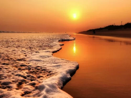 Chandrabhaga Beach Odisha golden hour sunset, featuring orange sun reflections waves sandy shore distant figures misty horizon, perfect beach experience for Konark Chandrabhaga tour package