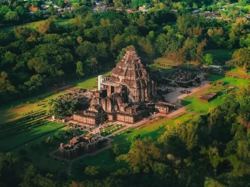 Aerial view of Konark Sun Temple Odisha during golden hour, featuring main shikhara tower, stone wheels, horses, lush forests, gardens, perfect heritage experience Odisha tour package.