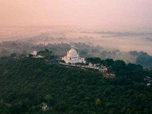 Dhauli Shanti Stupa at Bhubaneswar during misty sunrise, featuring white dome over Daya River valley, perfect heritage Bhubaneswar tour package.