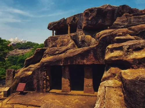 Udayagiri Caves Odisha multi-chamber rock-cut entrances rugged outcrop Jain temple background green trees blue sky, perfect Bhubaneswar heritage tour package.