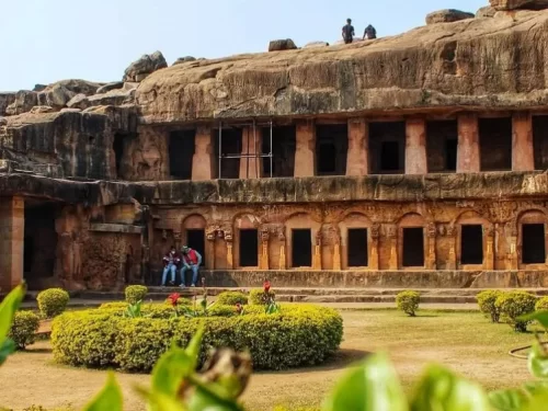 Udayagiri Caves Odisha Bagh Gumpha multi-cell rock-cut facade landscaped garden tourists blue sky, perfect Bhubaneswar Jain heritage tour package. 
