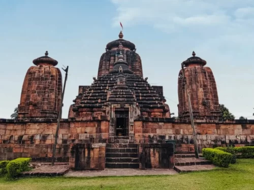 Brahmeswara Temple at Bhubaneswar on clear day, featuring three Kalinga spires and Odisha flag, perfect heritage Bhubaneswar tour package.