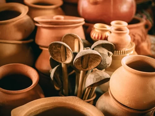 Warm earthy terracotta clay pots utensils spoons ladles stacked at Mapusa Market handicrafts stall North Goa India in rustic tones, perfect traditional Goan pottery kitchenware shopping experience with local market tour package. 