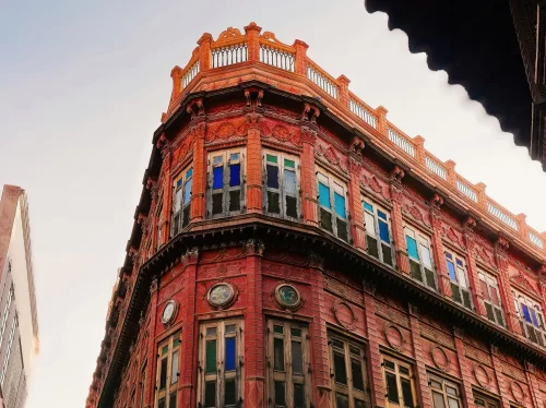 Rampuriya Haveli Bikaner Rajasthan overcast corner facade, featuring red brick building multicolored stained glass windows ornate balconies adjacent structures, perfect Rajasthan tour packages.