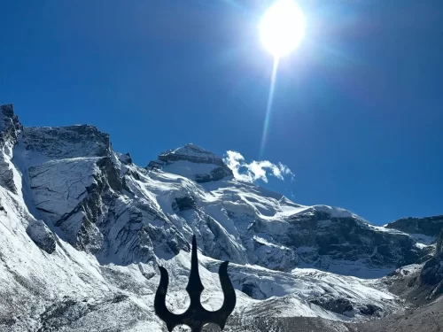Trishul silhouette at Adi Kailash during sunny day, featuring snow-capped Himalayan peaks and blue sky, perfect spiritual Adi Kailash tour package.