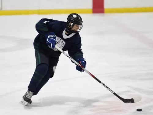 Ice Hockey player skating on an indoor ice rink while controlling the puck with a hockey stick during a match.