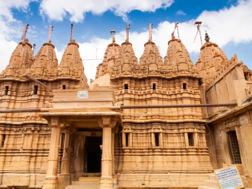 Sandstone Jain temple facade at Jaisalmer during blue sky, featuring ornate shikharas & arches, perfect romantic experience Rajasthan tour packages.