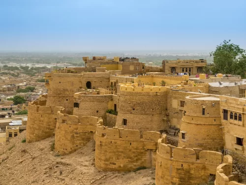 Curved bastions at Jaisalmer Fort during clear sky, featuring golden towers & cityscape, perfect adventure experience Rajasthan tour packages. 