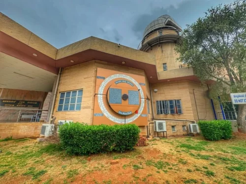 Jawaharlal Nehru Planetarium Bangalore side view during cloudy day, featuring sundial plaque, observatory tower and landscaping, perfect Karnataka tour package.
