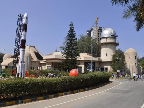 Jawaharlal Nehru Planetarium Bangalore entrance during sunny day, featuring rocket model, dome observatory and visitors, perfect Karnataka tour package.