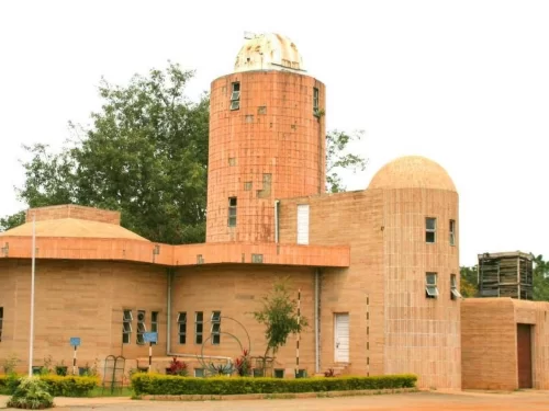 Jawaharlal Nehru Planetarium Bangalore exterior during sunny day, featuring distinctive terracotta dome and tower with greenery, perfect Karnataka tour package.