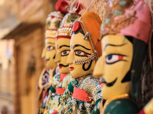 Close-up colorful Rajasthani puppets at Jodhpur Blue Corridor during sunset, featuring ornate attire and stone backdrop, perfect cultural experience in Rajasthan tour package. 
