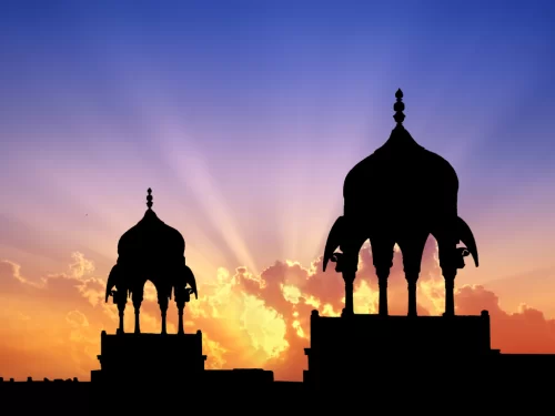 Junagarh Fort silhouette at Bikaner during vibrant sunset, featuring domed pavilions sun rays clouds, perfect romantic Rajasthan tour package. 