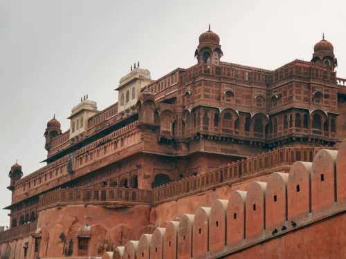 Historic facade of Junaghar Fort in Bikaner under cloudy sky, featuring red sandstone ramparts and balconies, perfect Bikaner heritage tour package