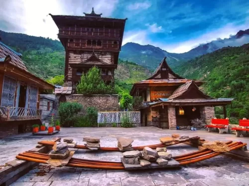 Kamru Fort Sangla Kinnaur Himachal Pradesh during partly cloudy skies, featuring tall multi-storey wooden tower temple complex lush green mountains courtyard benches, perfect cultural experience Himachal tour package.
