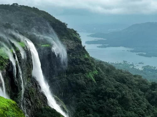 Waterfalls cascading from cliffs at King George Point in Matheran, Maharashtra, overlooking lush valleys and distant lakes during the monsoon, a scenic attraction included in Maharashtra tour packages.