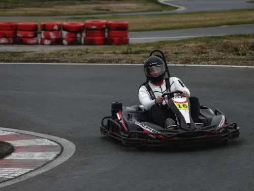 Go Karting person driving a go kart on a race track while wearing a helmet and protective gear around a sharp curve.