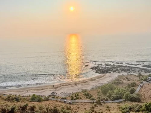 Sunset view over Korlai Beach in Maharashtra, with golden reflections on the Arabian Sea and a quiet shoreline below the hillside, a scenic coastal stop included in Maharashtra tour packages.
