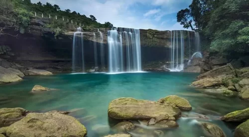 Krang Shuri Falls in Meghalaya, crystal clear turquoise pool beneath cascading waterfall cliffs.