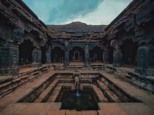 Ancient stone architecture of Krishnabai Mandir in Mahabaleshwar, Maharashtra, featuring carved pillars and a sacred water tank, a historic temple site included in Maharashtra tour packages. 