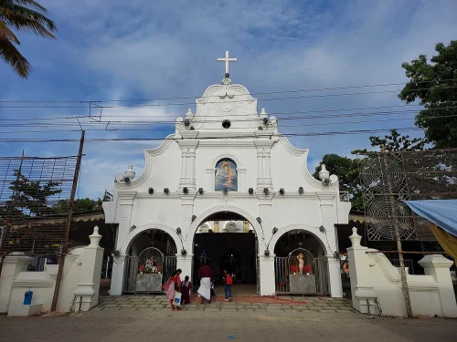 St. Mary's Church in Kudavechoor featuring classic white facade, ornate arched entrance, cross atop the structure, and peaceful courtyard, perfect spiritual experience with Kerala tour package. 
