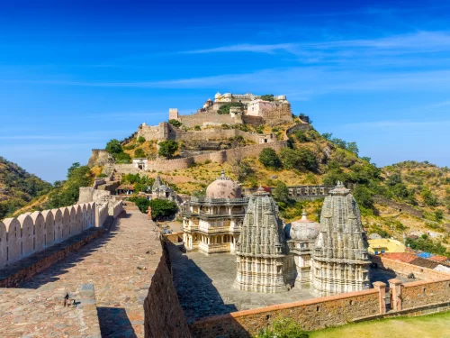 Kumbhalgarh Fort during sunny day, featuring towering walls, Jain temples, shikharas, hill backdrop, perfect adventure experience Rajasthan tour packages. 