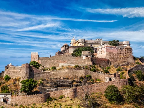 Kumbhalgarh Fort during partly cloudy sky, featuring multi-level palaces, bastions, dome tops, hillside setting, perfect adventure experience Rajasthan tour packages. 