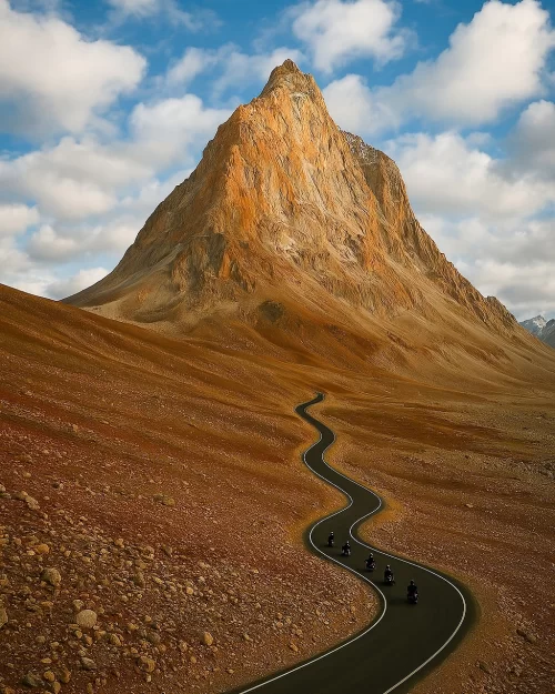 Winding mountain road leading to Gumbok Rangan peak in Zanskar Ladakh with bikers riding through rugged terrain, an adventure highlight in Ladakh tour packages