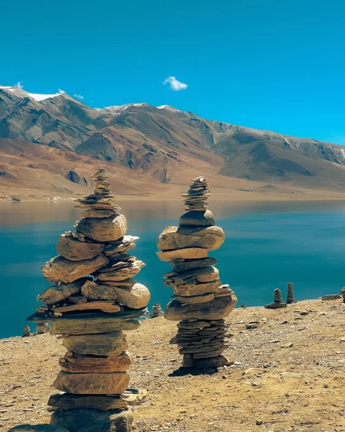 Stone cairns by Pangong Lake in Ladakh with crystal-clear blue waters and mountain backdrop, a scenic highlight in Ladakh tour packages