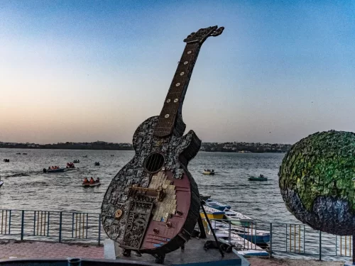 Giant guitar sculpture at Lake View in Bhopal, Madhya Pradesh, overlooking the water with boating activities in the background, a popular waterfront attraction featured in Madhya Pradesh tour packages