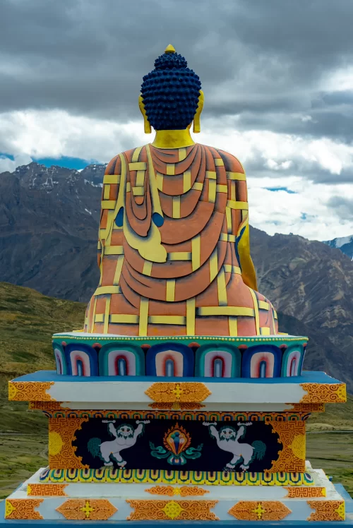 Colorful Buddha statue overlooking the rugged Himalayan landscape in Kaza, Spiti Valley, Himachal Pradesh, a serene high-altitude destination featured in Himachal Pradesh tour packages.