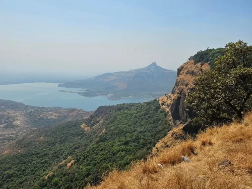 View from Little Chowk Point in Matheran, Maharashtra, overlooking lush valleys, rocky cliffs, and a distant lake, a scenic viewpoint featured in Maharashtra tour packages. 