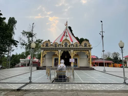 Mahabhairab Temple Tezpur during golden hour, featuring colorful striped temple dome gold ornate entrance white Shiva statue courtyard lamps trees, perfect cultural heritage Tezpur Assam tour package.