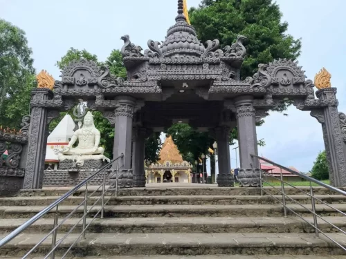 Mahabhairab Temple Tezpur during cloudy day, featuring ornate stone entrance gate white Shiva statue temple dome trees railings steps, perfect cultural heritage Tezpur Assam tour package.