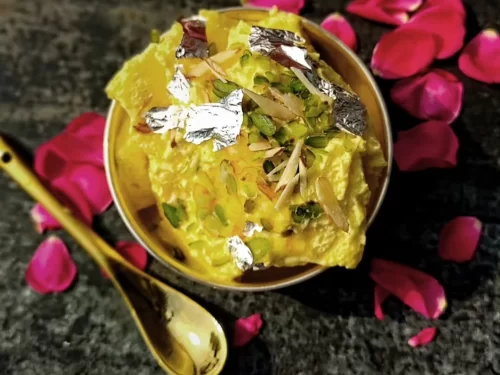 Makhan Malai, a light and creamy Indian winter dessert garnished with pistachios, almonds, and edible silver leaf.