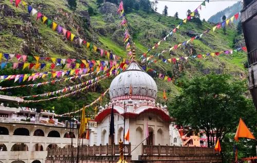 Colorful prayer flags over Manikaran Gurudwara dome during misty weather, featuring arched temple, green hills, perfect spiritual Himachal Pradesh tour package.