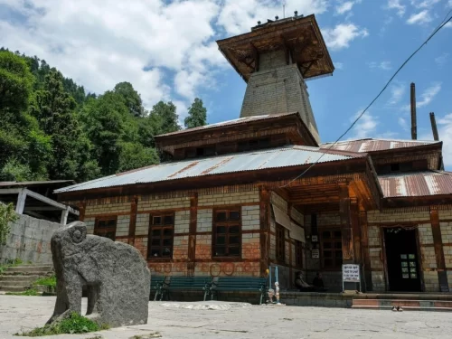 Manu Temple in Manali featuring traditional Himachali stone and wood architecture with a pagoda-style roof and scenic forested hills in the background.
