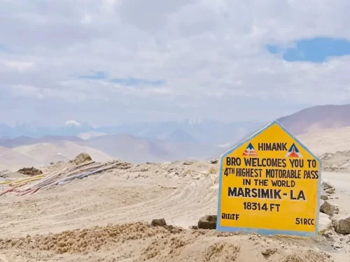 Marsimik La signboard Ladakh during clear partly cloudy day, featuring Himank BRO plaque 4th highest motorable pass 18314 ft, desert mountains, perfect adventure Ladakh tour package.