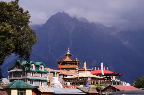 Hu-Bu-Lan-Kar Monastery at Kalpa during overcast skies, featuring prayer flags pagoda roofs snowy peaks trees, perfect spiritual experience Himachal tour package.