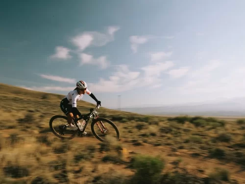 Mountain Biking rider speeding downhill on a rugged dirt trail across an open hillside landscape.