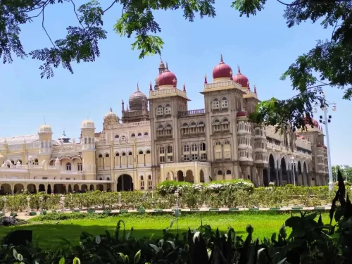 Mysore Palace majestic towers at Mysuru Karnataka during sunny day, featuring red domes yellow facade trees gardens framed branches, perfect royal heritage Karnataka tour package.
