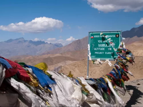 Namika La Pass signboard Ladakh India during clear partly cloudy day, featuring altitude marker prayer flags barren mountains highway, perfect high-altitude adventure Ladakh tour package.