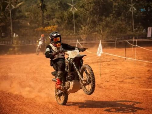 Off Road Biking rider performing a wheelie on a dirt track while wearing protective gear and helmet during an adventurous off road biking session.
