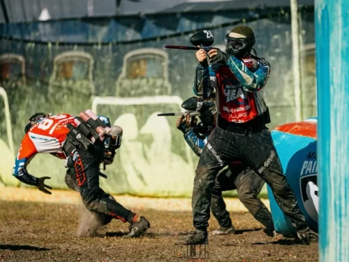 Paintball players in protective gear aiming and firing paintball guns while taking cover behind inflatable barriers during an intense outdoor paintball match.
