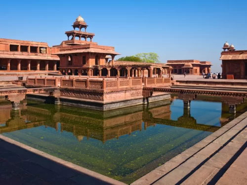 Panch Mahal at Fatehpur Sikri Uttar Pradesh during clear skies, featuring red sandstone pavilions, domes, arches, reflections in Anup Talab, perfect heritage experience Agra tour package.