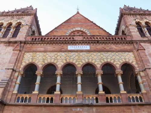 Prag Mahal main facade in Bhuj, Kutch during clear day, featuring Italian Gothic architecture with red sandstone arches, Corinthian columns, intricate jali work and PRAG MAHAL signboard, perfect heritage landmark with Gujarat tour packages.​